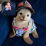 A cheerful baby sits like a tiny fashion boss on a blue couch, wearing a comically oversized trucker hat and a colorful outfit while flashing a smile that says the hat was absolutely their idea.