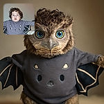 A wide-eyed toddler with curly hair and striking blue eyes is wearing a cute bat-themed outfit with wings spread out, looking curiously at the camera against a plain background.