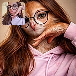 A young person with long hair and large round glasses strikes a playful pose, resting their chin on a hand while pouting lips slightly. They're wearing a light pink hoodie with some red text partially visible, set against a plain indoor background with a bright light source above.