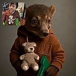A curious toddler with a pacifier attached to a teddy bear is holding two green toy water guns, standing in a warmly decorated room with a Christmas tree, stockings, and presents in the background, looking slightly to the side as if caught mid-thought.