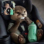 A cheerful toddler is buckled into a car seat, enthusiastically nibbling a frosty snack while a giant mint-green bottle photobombs the scene like it is auditioning to be the baby’s co-star. Sunlit scenery and the sturdy seat make this a very secure little road-trip portrait.