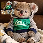 A tiny hoodie-wearing baby lounges like a pint-sized philosopher, tongue out and eyes half-dreaming, bundled on a cozy blanket against a leather couch — peak adorable indifference.