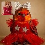 A cheerful little girl wearing a sparkling red dress adorned with stars and a big glittery bow headband smiles warmly at the camera while sitting against a plain beige wall.