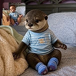 A curious baby sits proudly on a bed with a pacifier, striped fish shirt, and fuzzy blanket, looking like a tiny captain inspecting the bedroom while his socks prepare for a great escape.