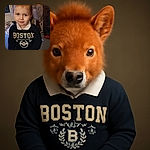 A charming young child with bright eyes and a slight smile wears a dark Boston sweatshirt with a white collar, standing indoors with a fan and various household items in the background.
