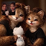 A cozy indoor selfie featuring a smiling young child and an adult, both with rosy cheeks and warm expressions, holding a white plush toy with a face sketch, set against a softly lit background.