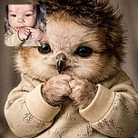A close-up photo of an adorable baby with curly hair, wearing a beige outfit with tree patterns, gazing curiously at the camera while clasping their tiny hands near their mouth.