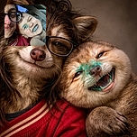 A close-up car selfie: an adult in glasses squeezes in while a little one grins like a mischievous marker bandit — blue scribbles decorate the child's nose and mouth as they squint and flash a big toothy smile, seatbelt visible and cozy chaos all around.