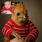 A bright-eyed baby in a red and white striped shirt beams joyfully while playfully holding an adult's hand, with a cozy indoor background featuring a couch and cushions.