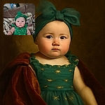 A chubby-cheeked baby wearing a bright green headband with a big bow and a matching green outfit, sitting on a couch covered with a patterned blanket featuring fish and other designs. The baby stares wide-eyed at the camera with a serious expression, creating an adorable contrast with the vibrant outfit.