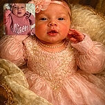 A cute baby dressed in a cozy pink knit sweater with the name 'Allison' embroidered on it, wearing a matching pink headband with a large flower, lying on a soft textured blanket and looking curiously at the camera.