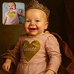 A joyful baby in a pink onesie with a shiny gold heart and the word 'love' beams a toothy grin while lying on a soft bed, radiating pure happiness and cuteness.