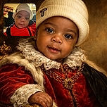 A close-up selfie of a curious baby wearing a cozy white beanie and a bright red jacket, with a softly lit living room in the background featuring a wooden shelf filled with cards and knick-knacks.