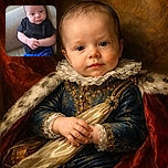 A cute baby dressed in a black shirt and blue shorts is sitting on a beige couch, looking curiously at the camera with hands clasped together, giving a calm and contemplative vibe.