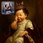 A peaceful baby with curly hair is sitting in a gray stroller, wearing a funny black shirt that says 'I was just supposed to be a backrub.' The baby has a relaxed expression with one hand gently touching their face, and the background shows a paved surface.