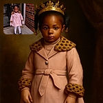 A little girl stands outside a building, dressed warmly in a stylish pink coat with leopard print accents, white tights, and black shoes. Her hair is adorned with colorful beads, and she looks curiously at the camera, framed by a brick wall and a glass door reflecting the surroundings.