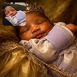 A peaceful sleeping baby wrapped in a cozy lavender and white outfit, nestled comfortably against a dark fabric background with a soft focus on the infant's serene face.