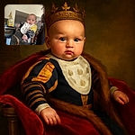 A chubby-cheeked baby is comfortably nestled in a gray baby carrier, wearing a striped yellow and navy sweater and a slightly stained bib, looking curiously at the camera as an adult partially appears on the right side of the frame in a casual indoor setting.