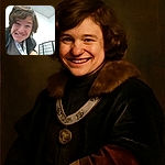 A cheerful young person with tousled hair leans close to the camera, flashing a wide, goofy smile in a brightly lit room with a folding screen and some posters on the wall.