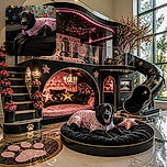 A cheerful black dog lounges dramatically across the couch in a pink patterned outfit, tongue out as if proudly modeling the latest canine pajamas. Behind it, floral upholstery and a starry blanket create the wonderfully chaotic set of a very cozy fashion shoot.