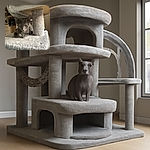 A curious gray kitten lounges on a soft, fuzzy cat tree platform, peeking out with alert eyes and delicate paws tucked beneath its body, basking in warm indoor light with a cozy kitchen background.