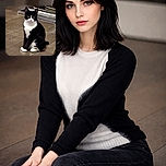 A poised tuxedo cat sits elegantly on a wooden floor, staring directly at the camera with curious eyes. The background includes some furniture and a reflective surface, adding depth to the cozy indoor setting.