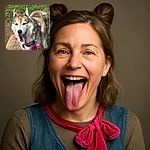 A happy husky with a big pink tongue hanging out, sporting a bright pink bandana with a bow, standing on a concrete slab with green grass in the background. The dog looks like it just finished a fun play session and is smiling for the camera.