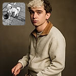 A fluffy dog on a leash looks back towards the camera with curious eyes, standing on a textured sidewalk next to a street bollard. The black and white filter adds a timeless charm to this casual urban stroll snapshot.
