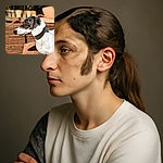 A close-up side profile of a dog with a striking multicolored face and blue eyes, standing outdoors against a rustic backdrop of wooden and clay elements, basking in the sunlight.