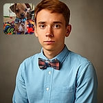 A charming little puppy wearing a stylish blue and brown plaid bow tie sits attentively on a vibrant floral bedspread, looking like the cutest guest at a fancy party in a cozy, lived-in room.