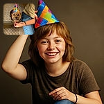 A happy small dog wearing a colorful party hat is sitting on a patterned floor next to a person in blue jeans and a beige shirt, with hands gently holding the hat in place, ready for a celebration.