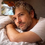 A cozy dog is resting its head on a white blanket, looking peaceful but a bit blurry and low-res, surrounded by warm wooden furniture.