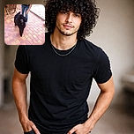 A very dignified black poodle stands on a terracotta-tiled patio, posing like it owns the place while a person's legs hover behind — clearly waiting for a treat or admiration. There's a water bowl at the edge and patio furniture in the background; the dog's curly fur and regal stance steal the show.