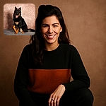 A strikingly handsome black and tan dog with fluffy fur is sitting on a grey surface against a textured brown backdrop, looking happy with its tongue playfully sticking out and one paw raised as if posing for a portrait session.