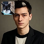 A close-up shot of a black and white cat with striking yellow eyes, peeking curiously over a green object with a blurred gravel background, capturing the cat's whiskers and attentive expression in sharp focus.