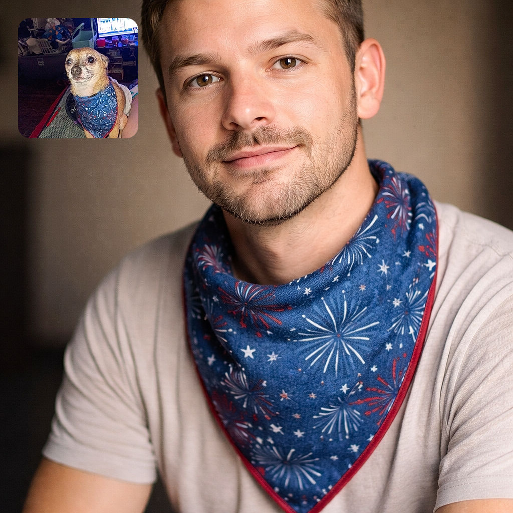 A small dog wearing a festive blue bandana with fireworks print sits attentively on a blanket indoors. The background shows a cluttered room with a TV screen displaying a bright scene, various household items, and a laundry basket. The dog's expression is calm and curious, illuminated by a strong light source.
