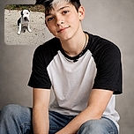 A cute black and white puppy sitting on a concrete surface with a curious and slightly tilted head, surrounded by some scattered leaves and greenery in the background.