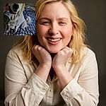 A fluffy golden retriever sits on a checkered bedspread, looking happy as a hand gently pets its cheek, capturing a candid moment of canine contentment indoors.