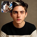 A curious black and white cat with big green eyes looks up close to the camera, sitting on a table covered with a patterned cloth and surrounded by various household items including a bottle, a spool of blue thread, and a leash.