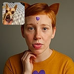 A small dog with big, soulful eyes and a tiny purple heart sticker on its forehead is being gently held by a hand. The dog sticks out its tongue slightly, adding a touch of adorable silliness, while the soft, blurred background of a bed creates a cozy atmosphere.