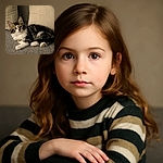 A fluffy tabby kitten lounges comfortably on a textured gray couch, with two cream-colored cushions behind it, gazing curiously at the camera with wide, innocent eyes.