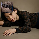 A tortoiseshell cat stretched out like a furry little loaf on a textured brown couch, completely relaxed and claiming the whole seat as its kingdom. A black cable snakes behind the cat adding a quirky touch to this cozy nap scene.