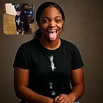 A happy black dog with white speckled paws and chest sits obediently on a brown carpeted floor, tongue out and ears perked up, with a cozy room background featuring a wooden nightstand, a lamp, and some household items.