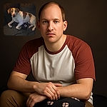 A cozy dog lounges on a dark couch with a paw-print pillow, looking curiously at the camera with a slight glow in its eyes from the flash.