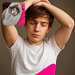 A cozy cat is stretching and curling its paws above its head, looking like it's meditating or practicing yoga on a comfy lap with bright pink shorts and a soft maroon blanket in the background.
