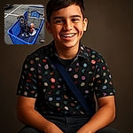 A happy puppy wearing a colorful shirt sits comfortably inside a blue shopping cart in a parking lot, surrounded by a few toys and a long receipt, with a person's feet visible nearby.