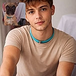 An impossibly earnest French bulldog puppy stares straight into the camera with giant bat ears, a teal collar, and a face full of serious questions about snacks and naps — background shows a potted plant, a draped sheet, and a cozy blue blanket at the bottom.