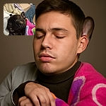 A cozy little French Bulldog puppy snuggled up in a colorful blanket, looking adorably sleepy with its tongue slightly sticking out, resting comfortably on a person's lap.