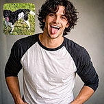 A happy black and white dog stands on a grassy field with its tongue hanging out, looking playful and energetic on a sunny day.
