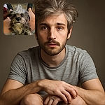 A scruffy little dog with a wild tuft of hair on its head stares curiously at the camera while comfortably nestled on a person's lap, with the person's legs and slippers visible in the background, giving a cozy indoor vibe.